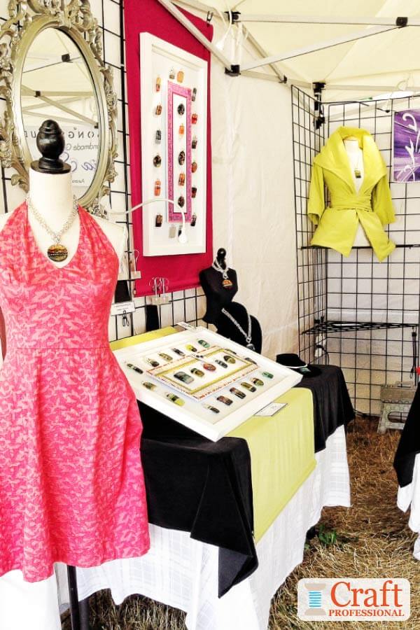 The mannequin at the front of this booth helps to attract attention and draw customers into the booth. Mannequin in a pink dress displaying handmade pendant at a craft show.