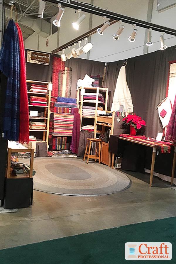 Handmade textiles displayed in a craft booth. Lights are secured overhead with approximately on light per foot.