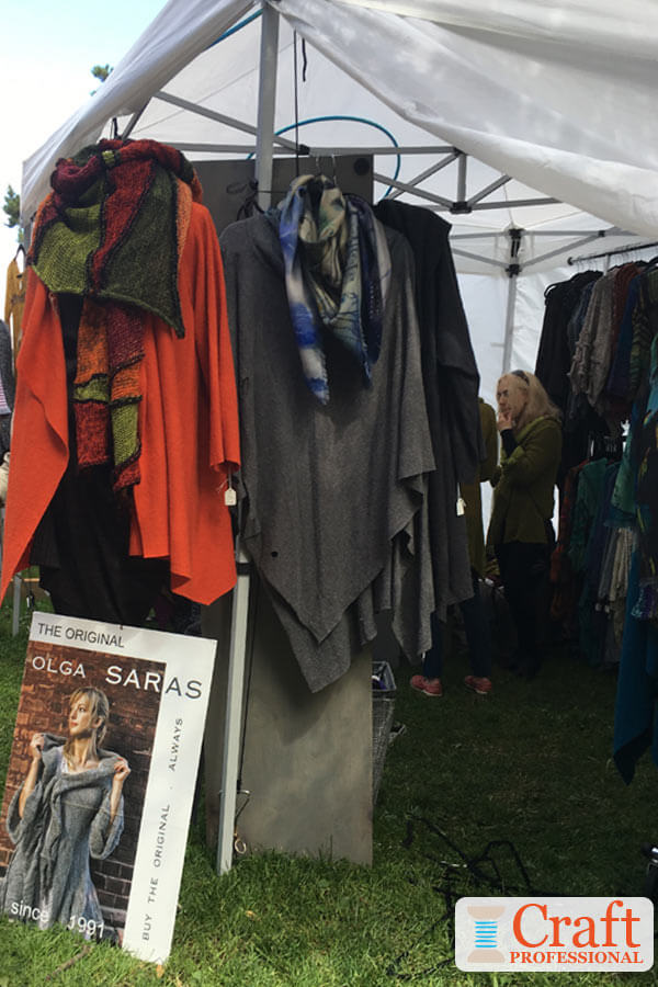 Handmade clothing in a portable tent at an outdoor craft show. A hula hoop is between the canvas canopy and tent frame to prevent water from pooling on the tent.