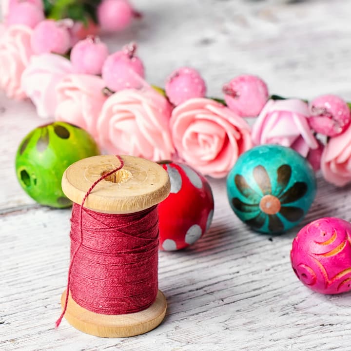 Colorful thread and hand-painted beads arranged on a wooden craft table, ready for making handmade jewelry or crafts. Colorful thread and hand-painted beads arranged on a wooden craft table, ready for making handmade jewelry or crafts.