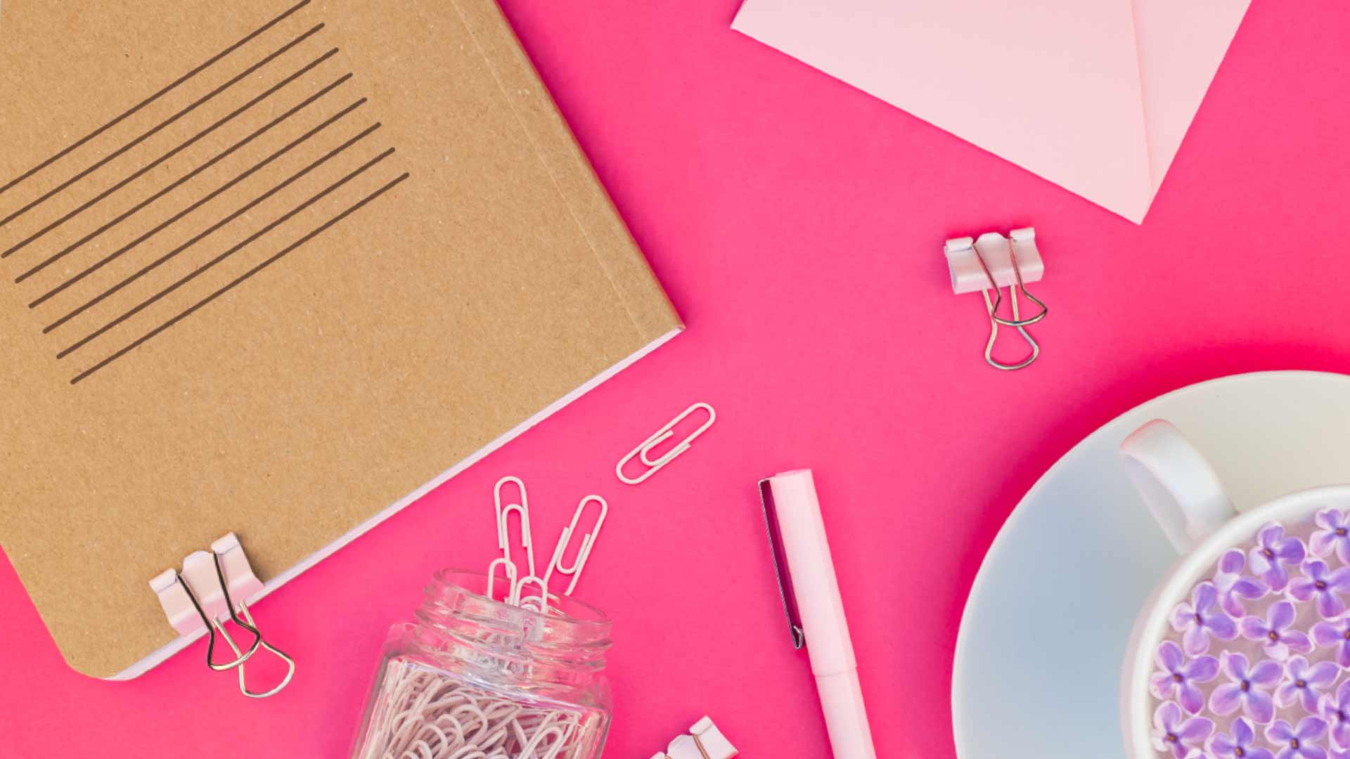 Pink workspace with notebook, paperclips, and floral tea. Pink workspace with notebook, paperclips, and floral tea.