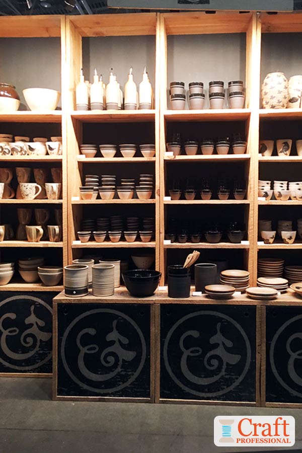 This handmade pottery display demonstrates the importance of avoiding overcrowding your craft booth. Click through for 6 more examples of visual merchandising techniques at craft shows. Handmade black and cream tableware displayed on tall wooden shelves at a craft show demonstrates the important of avoiding overcrowding your booth.