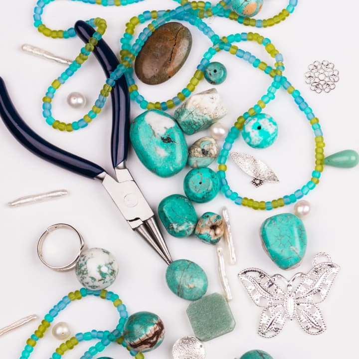 Turquoise beads, pliers, and jewelry-making tools arranged on a work surface, ready for creating handmade accessories. Turquoise beads, pliers, and jewelry-making tools arranged on a work surface, ready for creating handmade accessories.