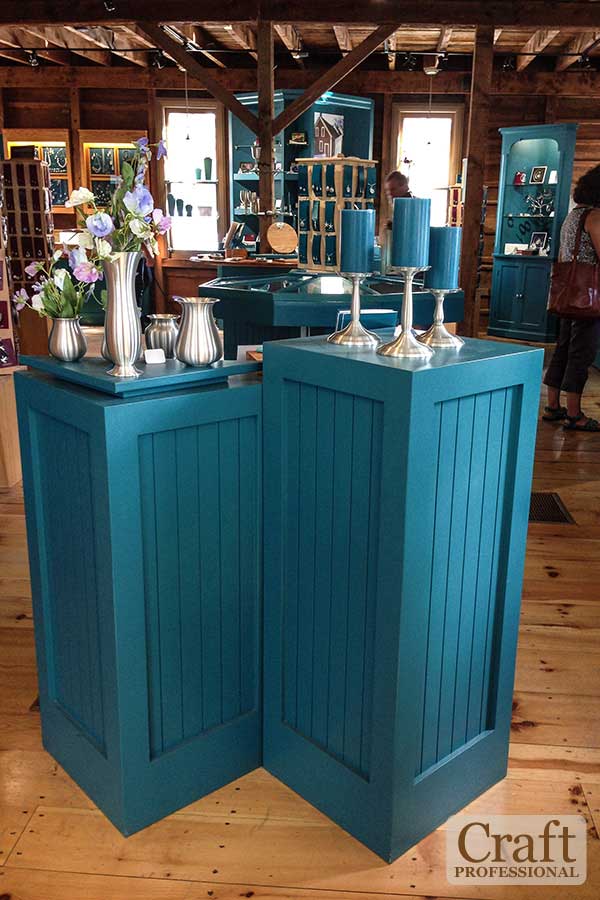 Handmade pewter candlesticks displayed on colorful pedestals