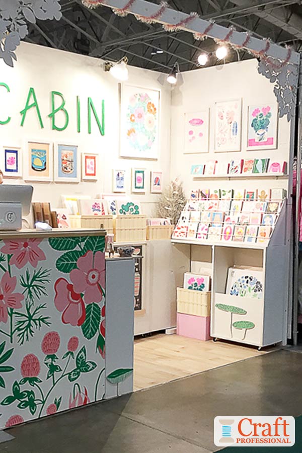 This  craft booth is bright but uses a restrained color scheme, that works with the art prints and cards on display. Click through for 6 more craft booth photos showing visual merchandising techniques Art prints and cards on display at a craft show in a bright pink, green, and white booth.